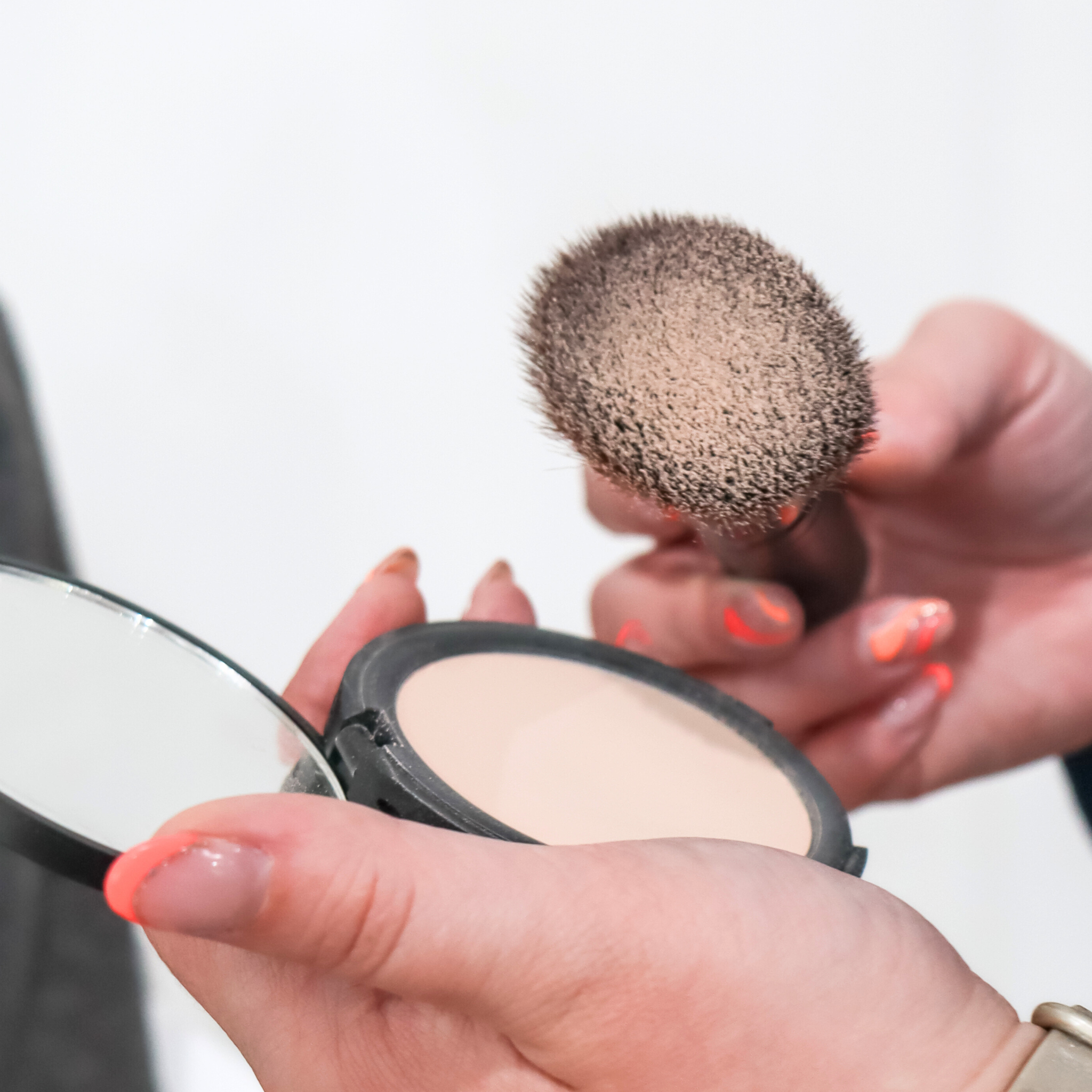 Hands hold face powder compact and makeup brush, preparing for cosmetic application.
