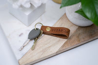 Keys dangle from a leather keychain with "Urban Southern" embossed on it, resting on a modern marble and wood tray.
