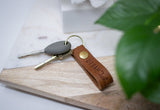 Keys with a stylish Urban Leather keychain rest on a modern wooden and marble tray.
