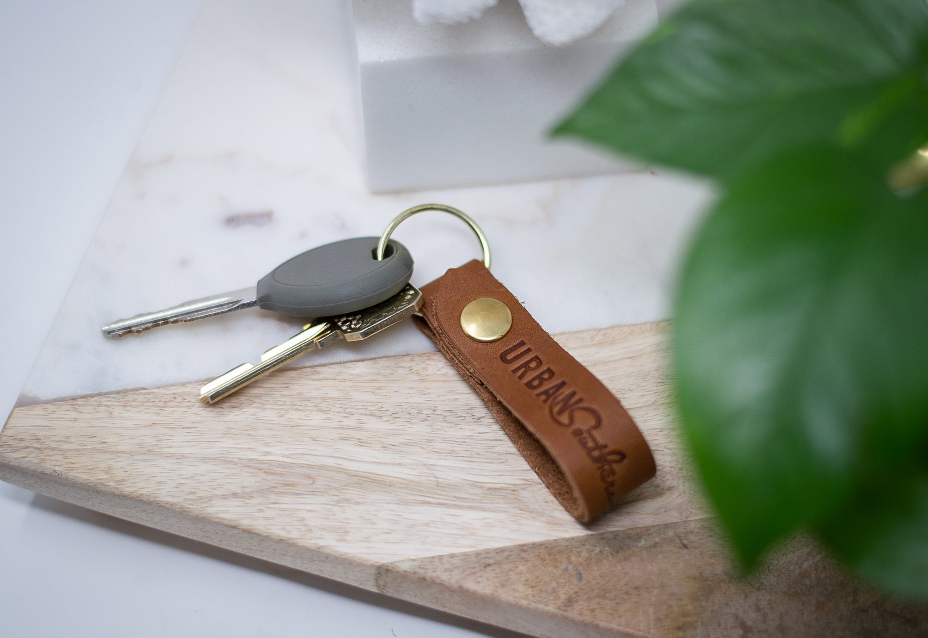 Keys with a stylish Urban Leather keychain rest on a modern wooden and marble tray.
