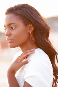 African-American woman models a teardrop-shaped leather earring and a cream-colored sweater, gazing toward a sunlit horizon.