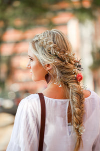 Blonde woman showcases a beautiful floral braided hairstyle with baby's breath and a peach rose.

