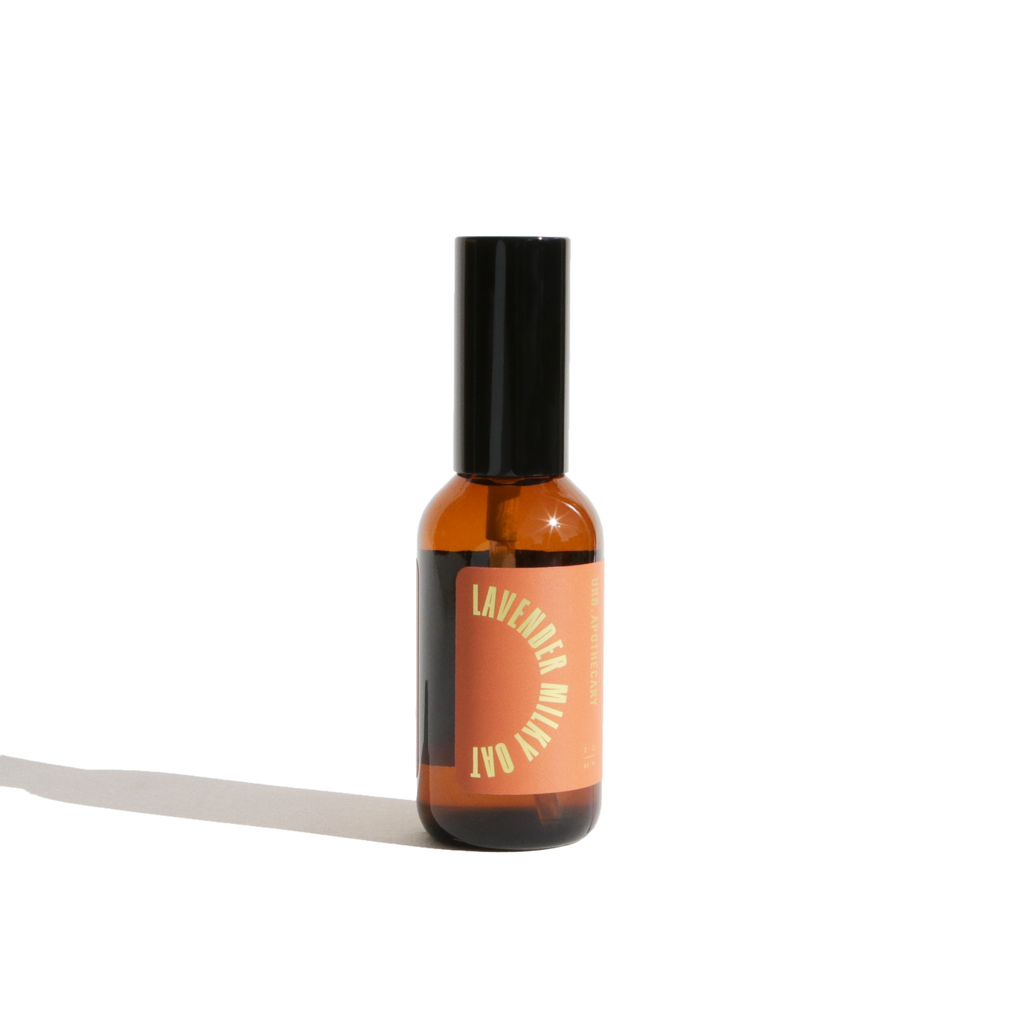 Still life shows an amber glass bottle of lavender milky oat aromatherapy spray against a white background.

