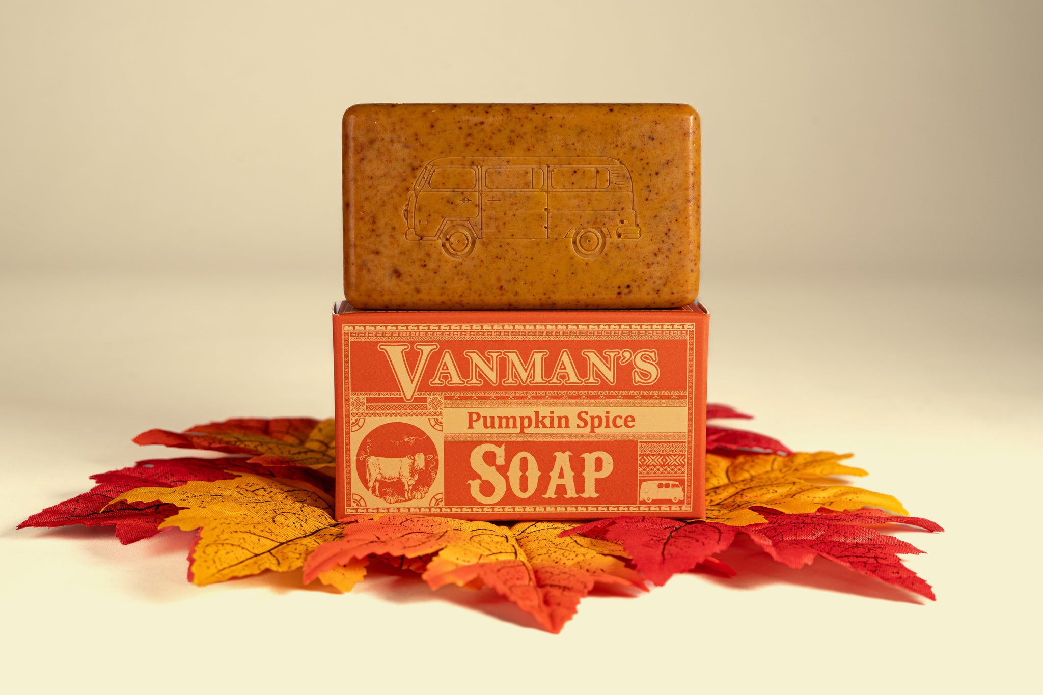 Vanman's Pumpkin Spice Soap bar, embossed with a VW bus, rests on its box surrounded by autumn leaves.
