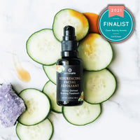 Annmarie Resurfacing Facial Exfoliant, a 2021 Clean Beauty Awards finalist, sits surrounded by cucumber slices and amethyst on a marble surface.
