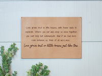 A farmhouse style decor sign displays the quote, "Love grows best in little houses," on a rustic tan background with greenery accents.
