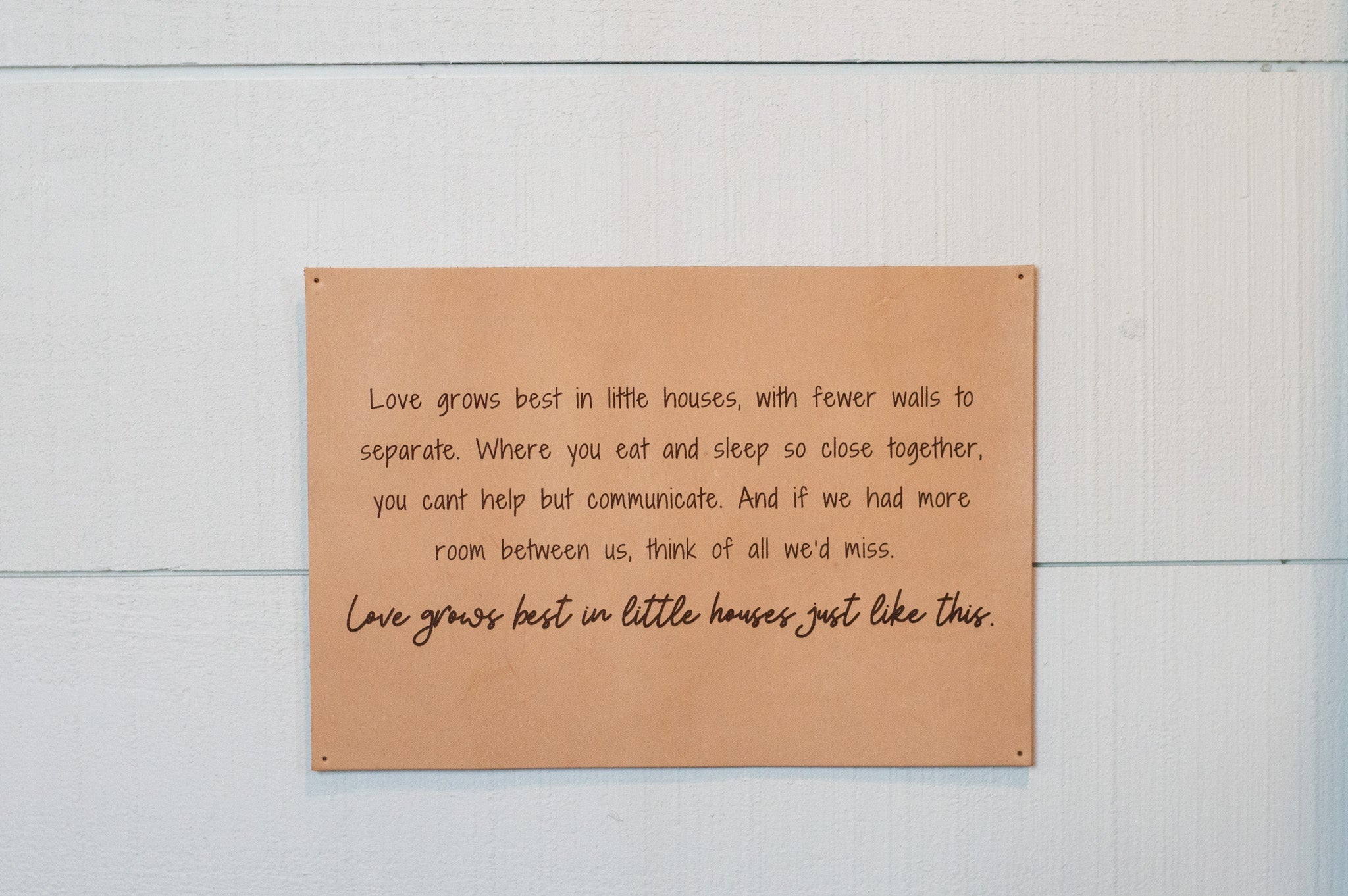 Wooden wall displays an inspirational quote about love growing in small homes, emphasizing family and togetherness.
