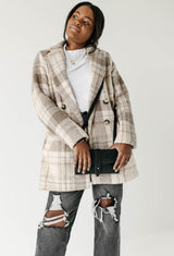 A Black woman models a plaid coat, ripped jeans, and a black crossbody bag in a fashion studio.
