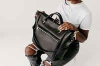 Woman holds a luxury black leather tote bag, showcasing its craftsmanship and versatile design.
