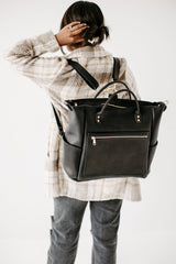 Woman wearing a stylish black leather backpack adjusts her hair.
