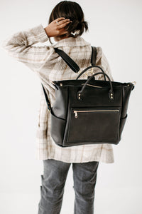 Woman wearing a stylish black leather backpack adjusts her hair.
