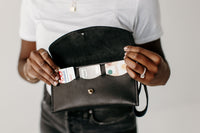 A woman displays her stylish black leather wallet, showcasing credit cards from Costco, Amazon Prime Visa, and Starbucks.
