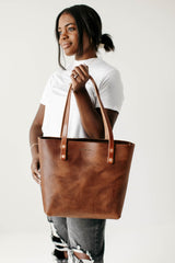 A smiling Black woman models the Urban Southern handmade leather tote bag.
