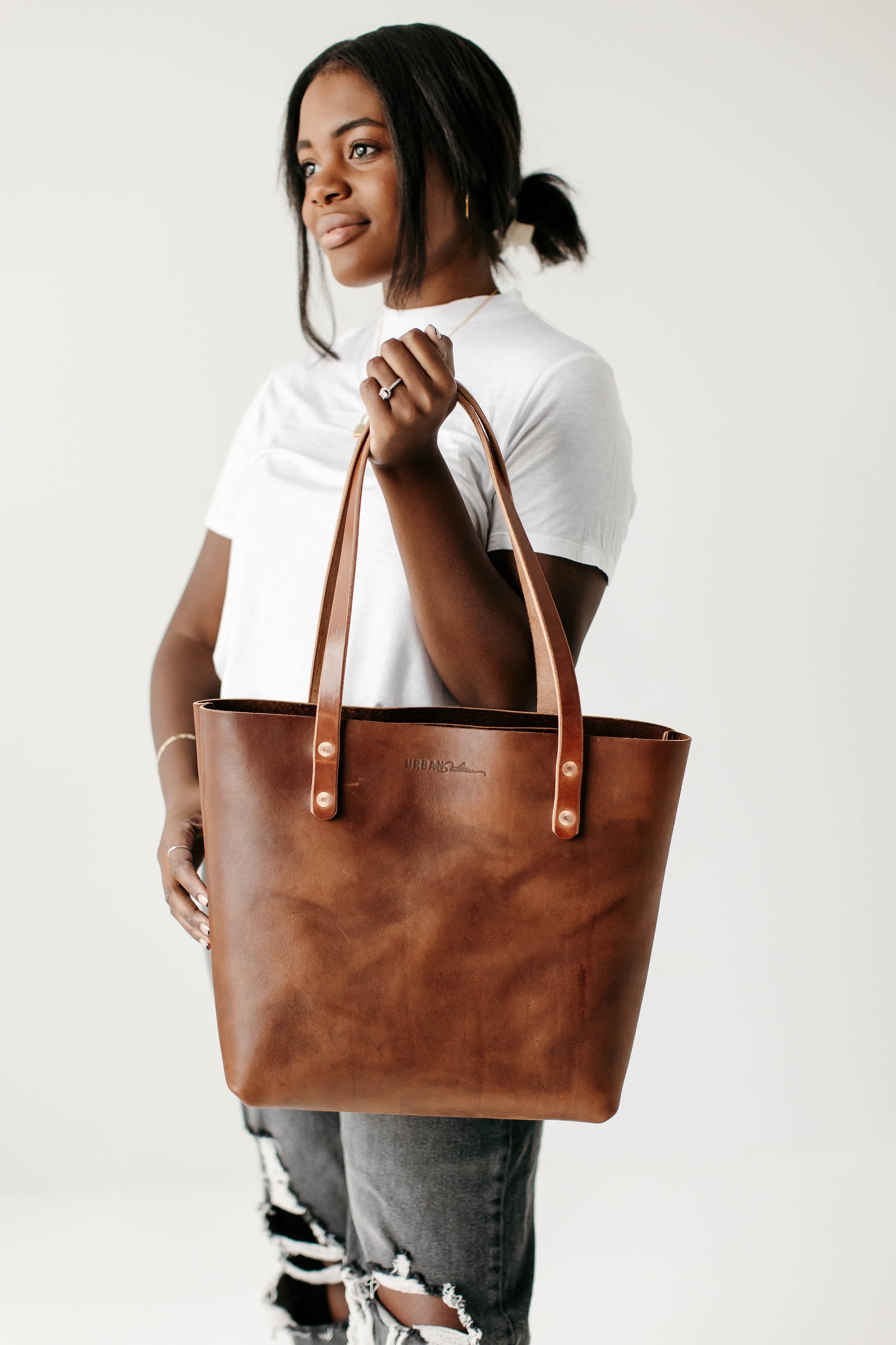 A smiling Black woman models the Urban Southern handmade leather tote bag.
