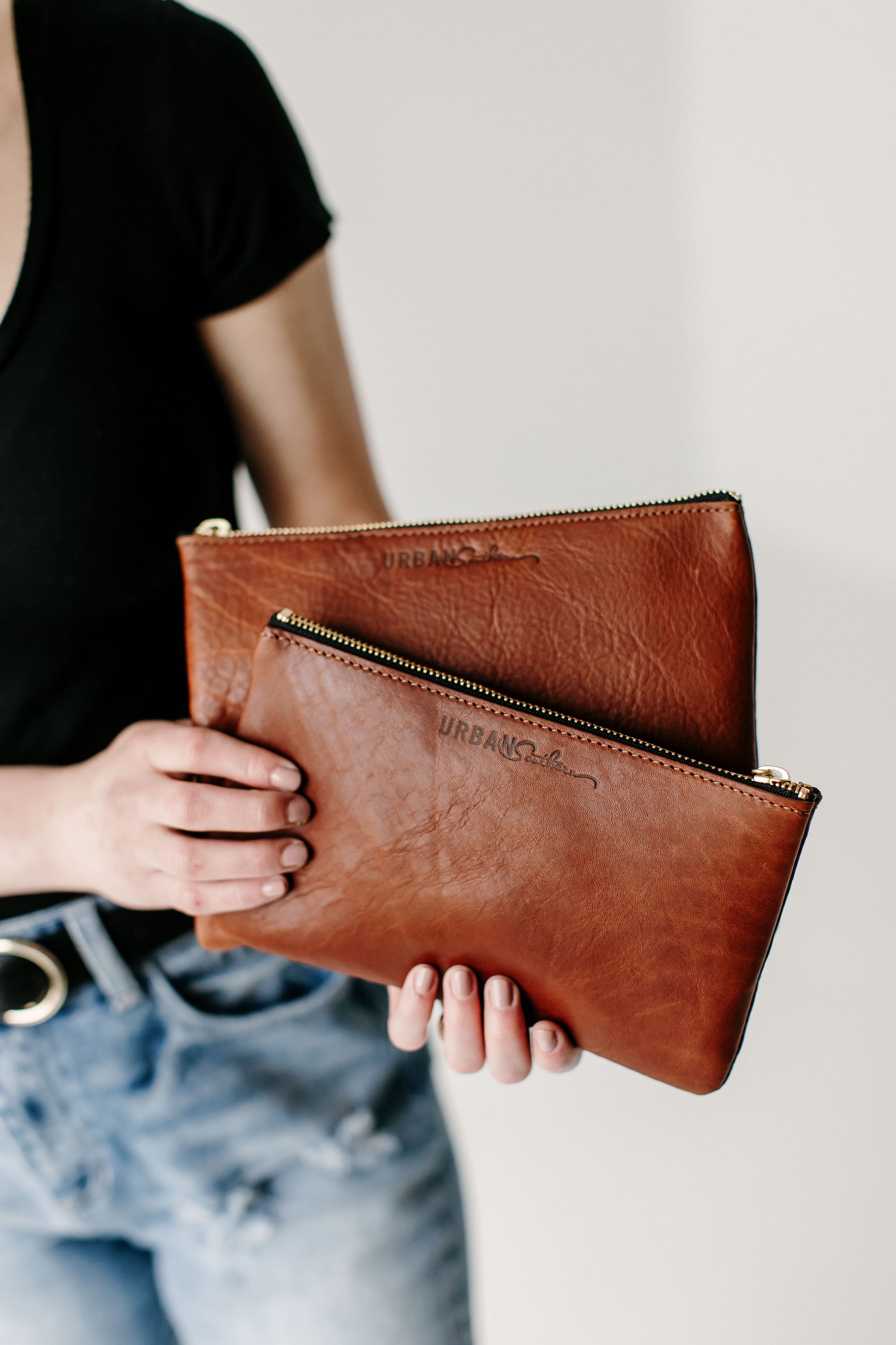 A person holds two brown leather Urban Southern zipper pouches.
