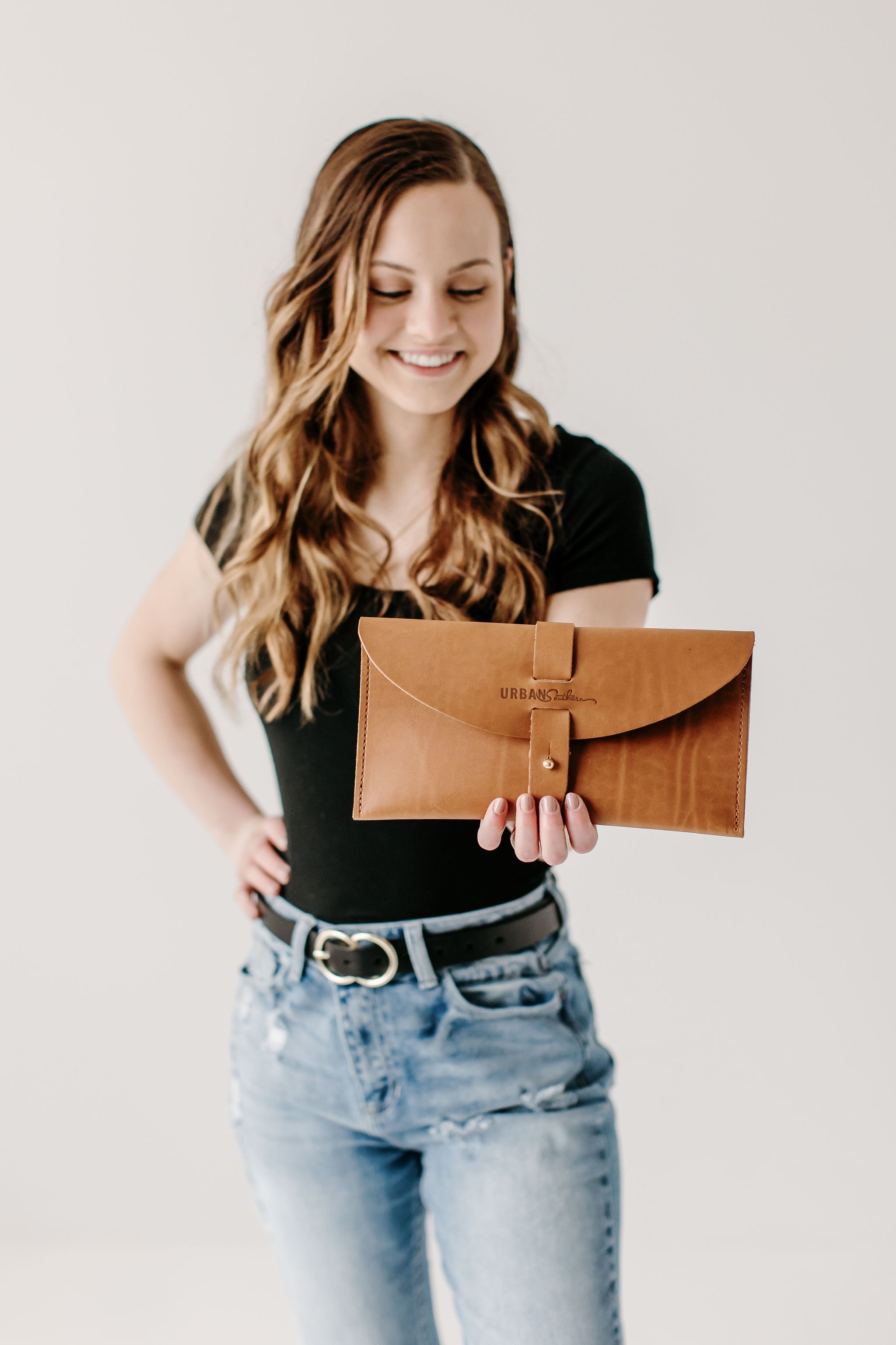 A smiling woman showcases an Urban Southern leather clutch wallet.
