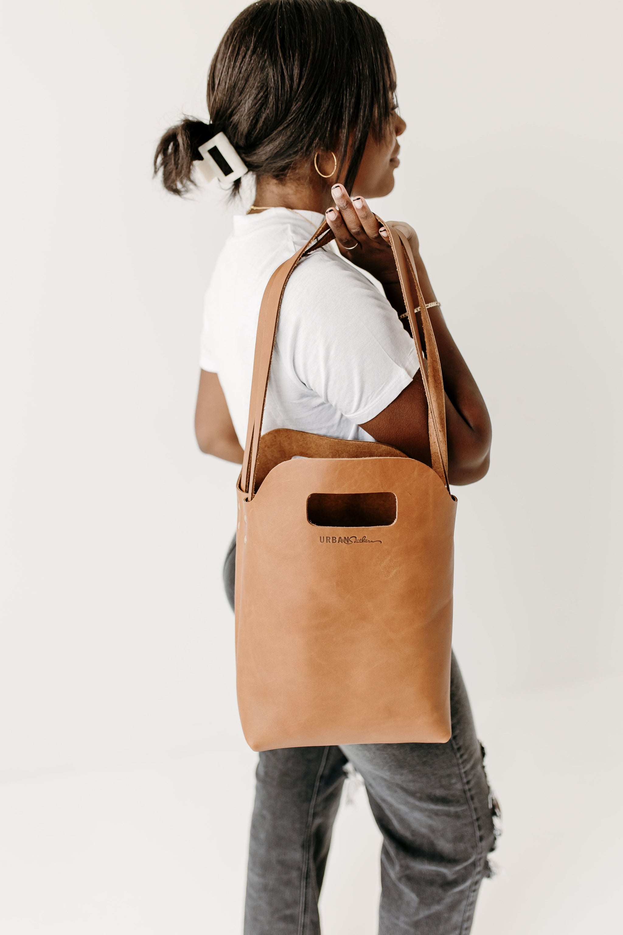 Woman carries an Urban Southern leather tote bag over her shoulder, showcasing its minimalist design.
