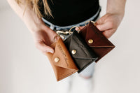 Hands display three leather keychains, each a different color, from Urban Southern.
