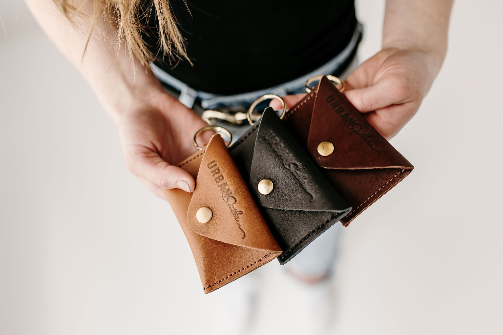 Hands display three leather keychains, each a different color, from Urban Southern.
