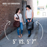 Two models demonstrate the size and style of large leather tote bags in a narrow alleyway, comparing a 5' and a 5'7" model.
