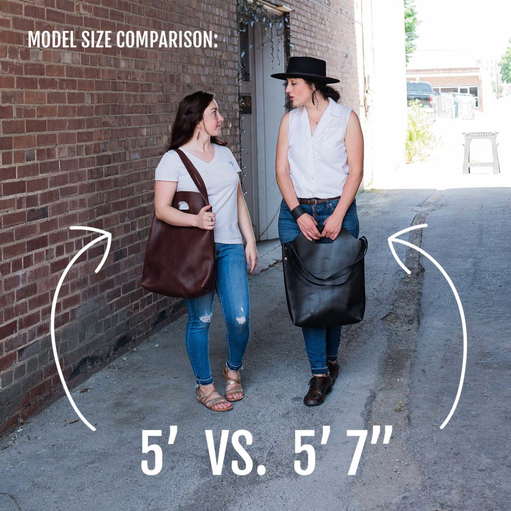 Two models demonstrate the size and style of large leather tote bags in a narrow alleyway, comparing a 5' and a 5'7" model.

