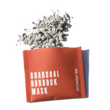 Urb.Apothecary's charcoal burdock mask packet lies beneath a pile of its grey, powdery contents.
