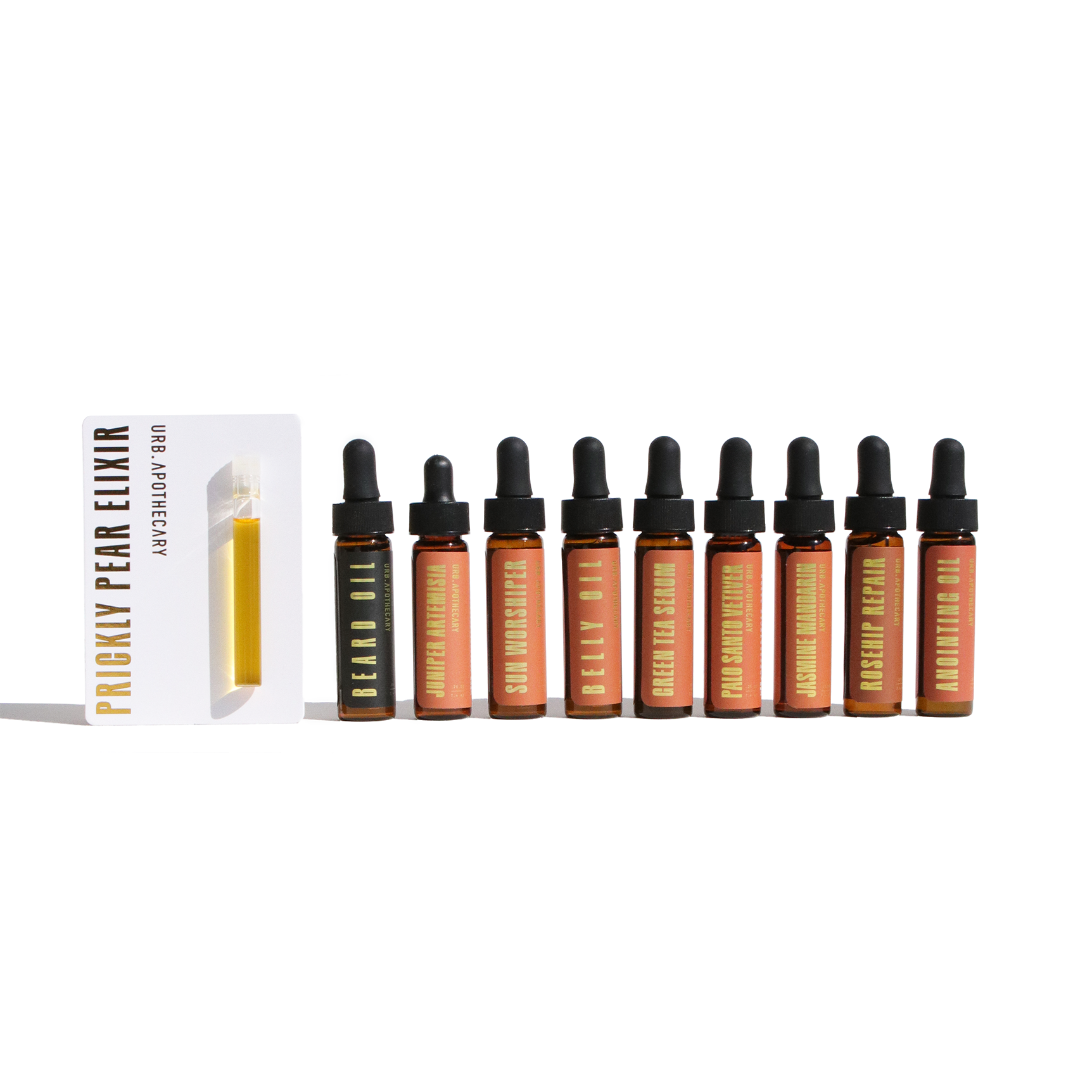 Urb Apothecary displays a collection of natural beauty oils, including Prickly Pear Elixir, Beard Oil, and Green Tea Serum, in amber glass bottles with dropper tops.
