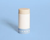 Showcasing a plastic-free deodorant balm in a paper tube, decorated with blue vans on a polka-dot background.
