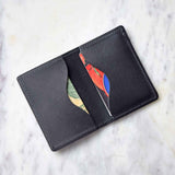Close-up reveals a black leather wallet displaying a colorful card and folded cash on a marble surface.

