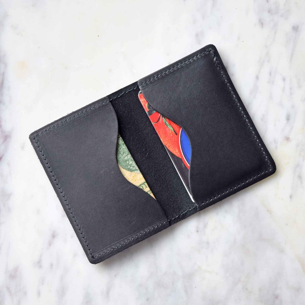 Close-up reveals a black leather wallet displaying a colorful card and folded cash on a marble surface.
