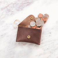 A brown leather coin purse spills loose change onto a marble surface.
