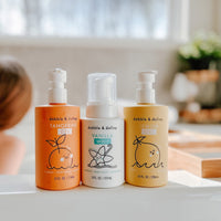 A child soaks in a tub near Dabble & Dollop kids' bath products including tangerine gel, vanilla whip, and lemon gel body wash and shampoo.