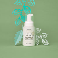 Dabble Ducky infant wash bottle sits among decorative paper leaves, promoting a fragrance-free delicate cleanser for newborns.

