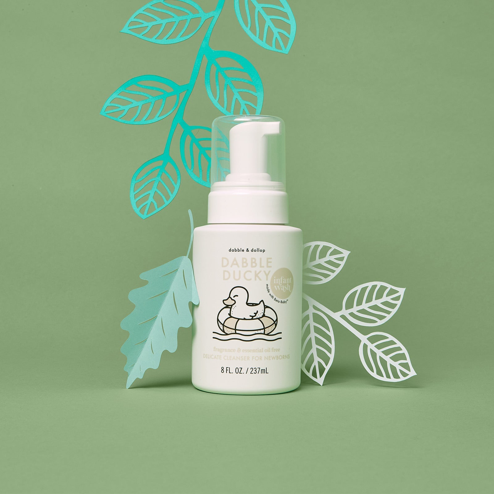 Dabble Ducky infant wash bottle sits among decorative paper leaves, promoting a fragrance-free delicate cleanser for newborns.
