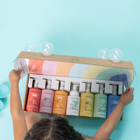 A child opens a colorful box of Dabble & Dollop natural bath products, featuring fun fruit-themed body wash and shampoo gels.
