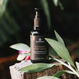 Annmarie Activated Night Serum sits atop a weathered wood block surrounded by green foliage, promoting natural skincare.
