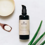 Annmarie Aloe Herb Cleanser sits with a scoop of cream and aloe leaves, promoting organic facial care.
