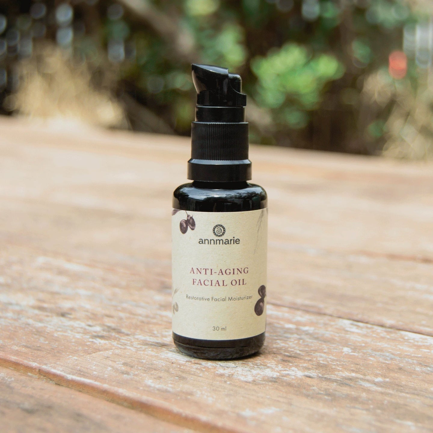Annmarie Anti-Aging Facial Oil bottle sits on a wooden surface in an outdoor setting.
