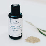 Annmarie Ayurvedic facial scrub bottle sits beside a pile of its dry herb exfoliant powder.
