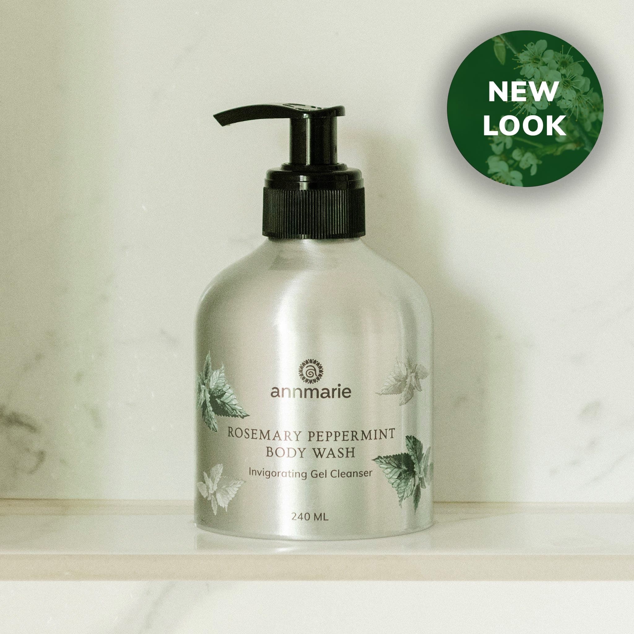 Annmarie's new rosemary peppermint body wash in a silver bottle sits on a marble shelf.

