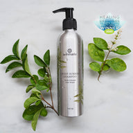 Annmarie Sweet Sunrise shampoo, an Earth Day Beauty Award winner, sits among green leaves on a marble surface.
