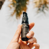 A hand holds Annmarie Fruit Ceramide Eye Serum against a bright, outdoor background.
