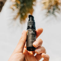 A hand holds Annmarie Fruit Ceramide Eye Serum against a bright, outdoor background.
