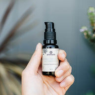 A hand holds a bottle of Annmarie Herbal Facial Oil, an unscented moisturizer for sensitive skin.
