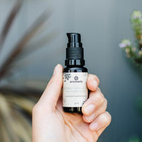A hand holds a bottle of Annmarie Herbal Facial Oil, an unscented moisturizer for sensitive skin.
