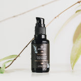 Annmarie's black Hyaluronic Acid and Peptides elixir bottle promotes skin hydration against a botanical backdrop.
