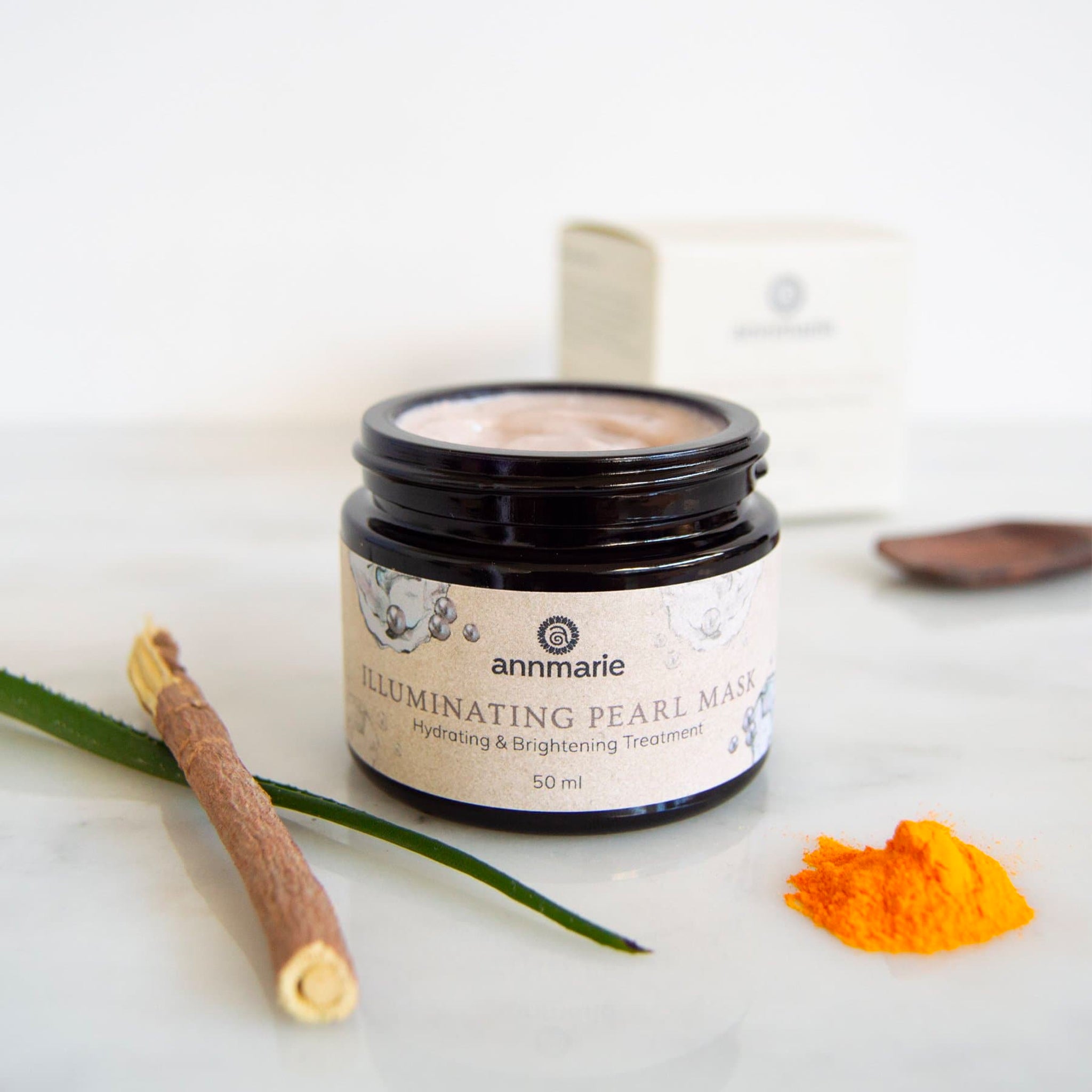 Annmarie Illuminating Pearl Mask sits alongside turmeric powder, aloe vera, and a miswak stick, showcasing natural skincare ingredients.
