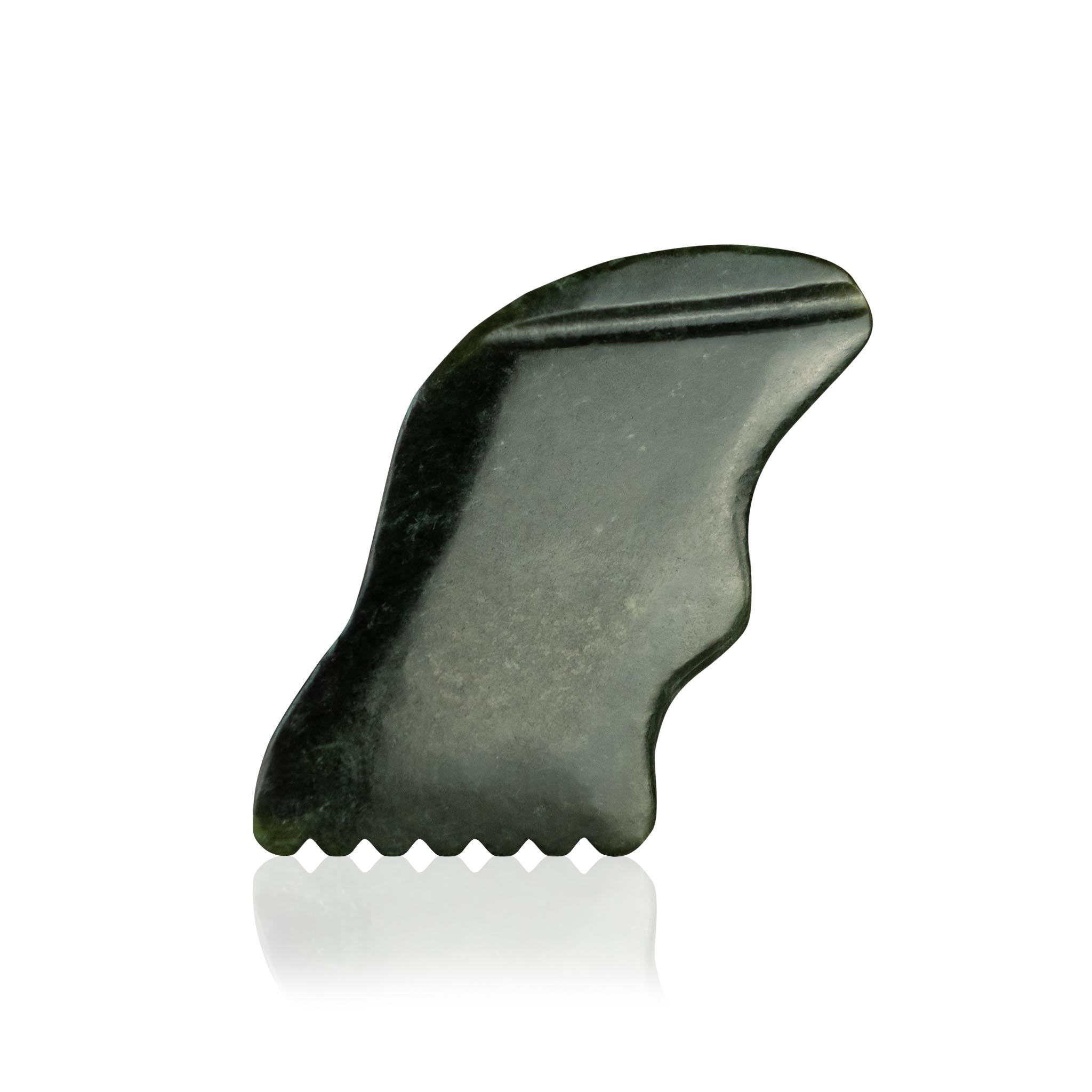 A jade gua sha tool with a toothed edge rests on a reflective white surface.
