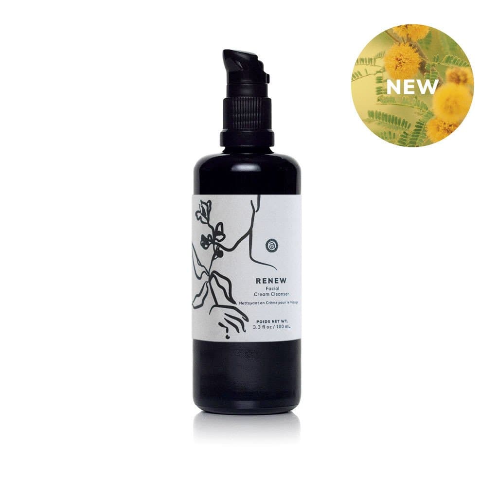 A black bottle of Renew Facial Cream Cleanser sits on a white surface, featuring a floral design and a "NEW" badge with yellow flowers.
