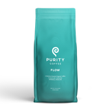 A turquoise bag displays the Purity Coffee logo, advertising their Flow medium-roasted organic whole bean coffee blend.
